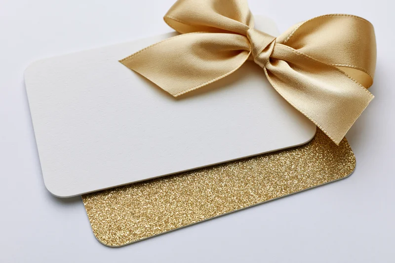 Two stacked gift cards with a gold ribbon bow on white background