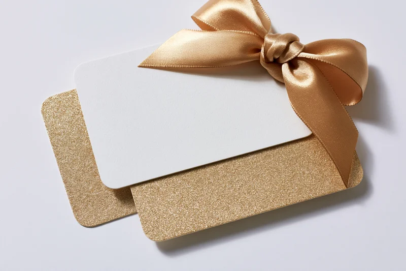 Two stacked gift cards with a gold satin ribbon bow on white background