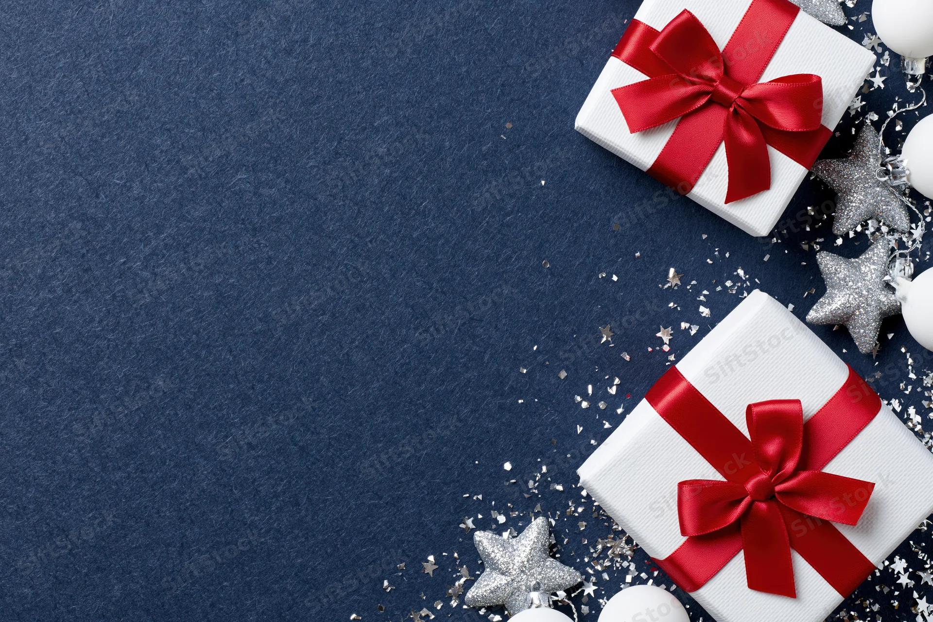 Two white gift boxes with red satin bows and silver stars on blue surface with copyspace