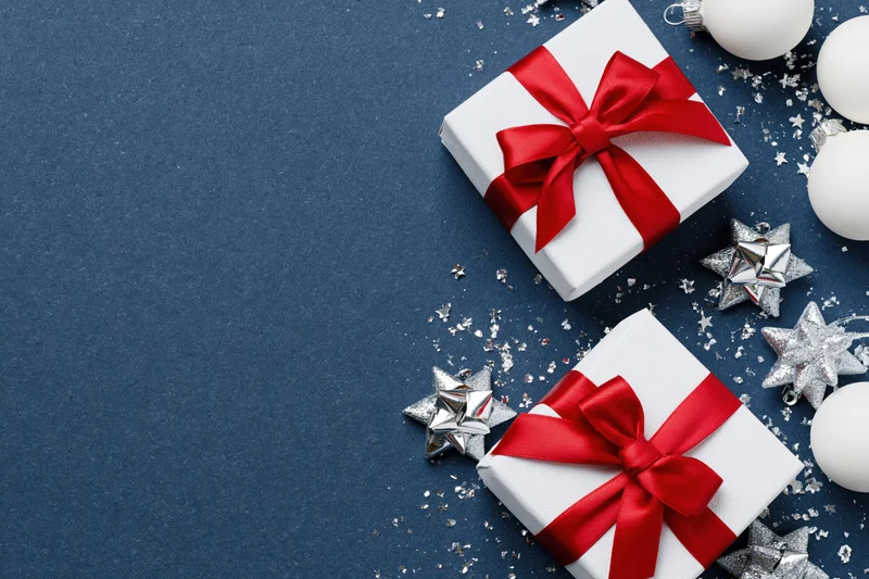 Two white gift boxes with red satin bows and silver star ornaments on blue surface