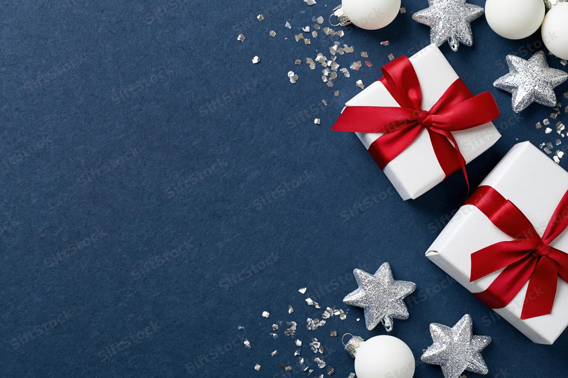 Two white gift boxes with red ribbons and bows on blue background with silver stars and confetti