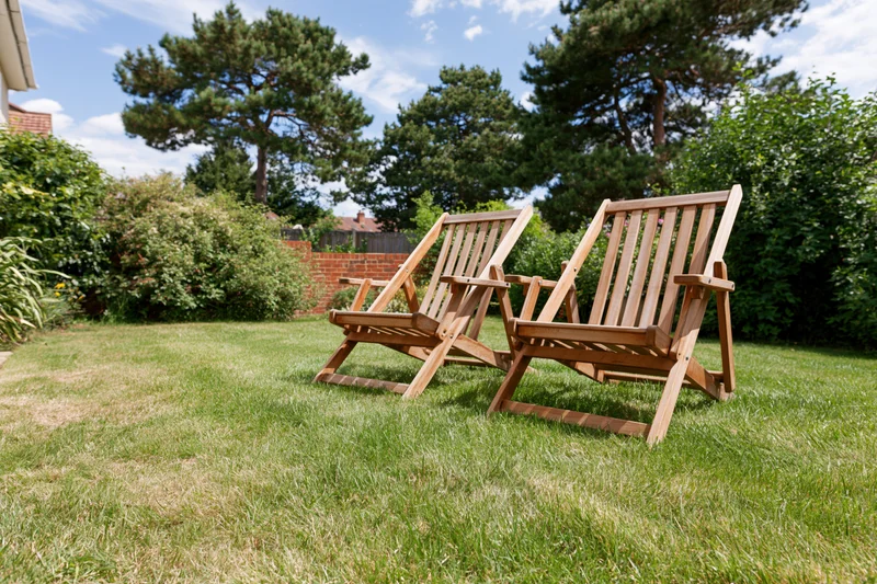 Two wooden deck chairs reclining on a green lawn in a garden backyard