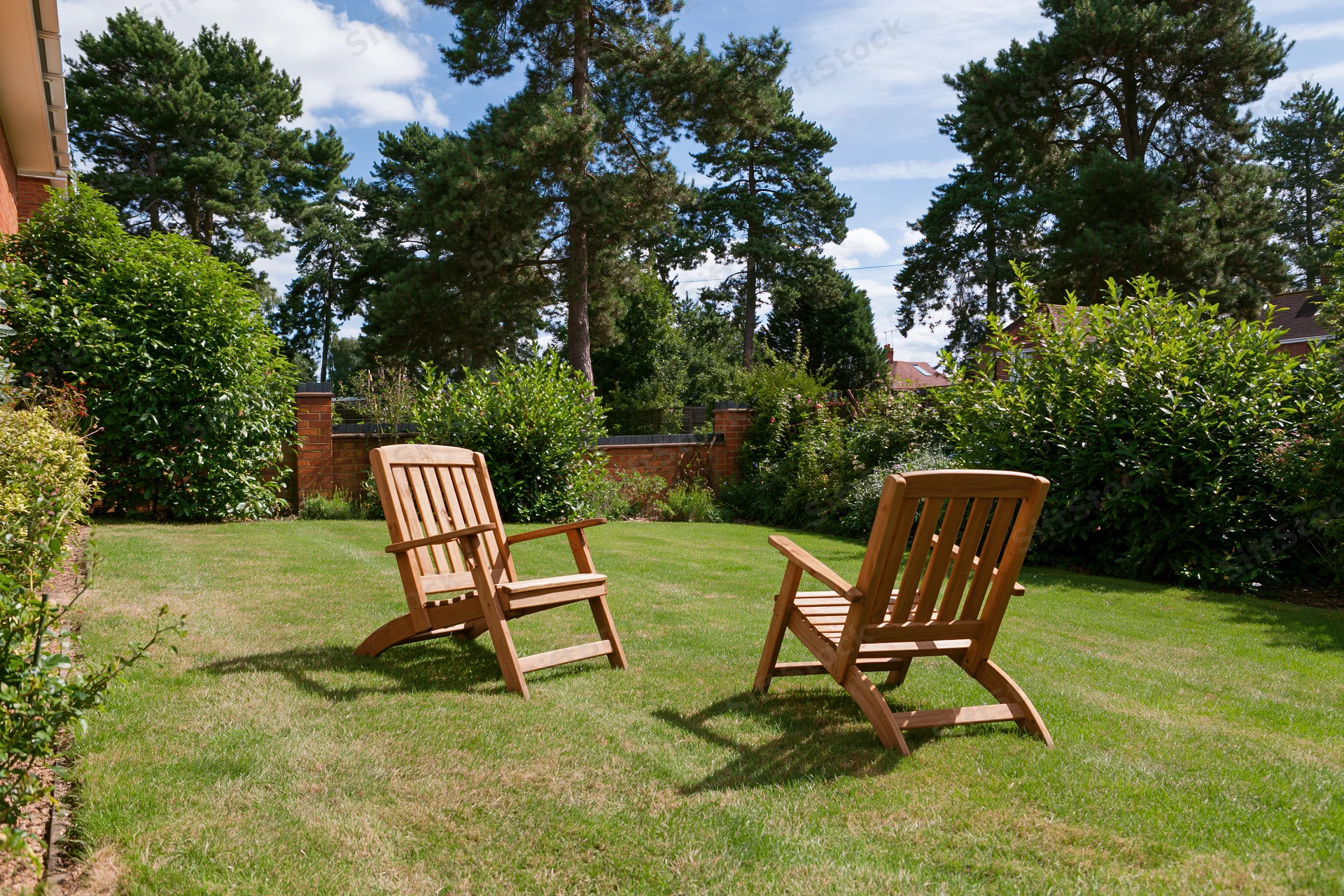 Two wooden deck chairs on a neatly trimmed green lawn in a private garden
