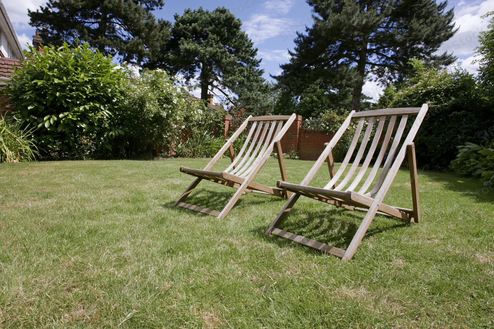 Two wooden deck chairs resting on a neatly trimmed green lawn in a garden setting