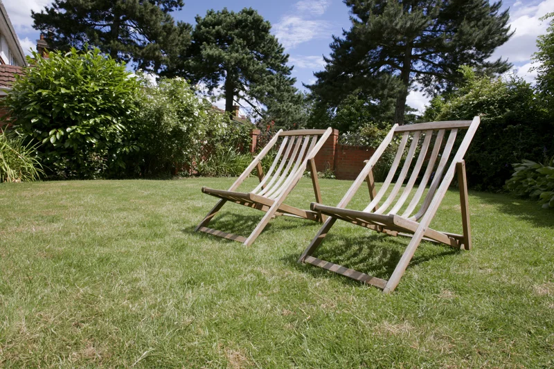Two wooden deck chairs resting on a neatly trimmed green lawn in a garden setting