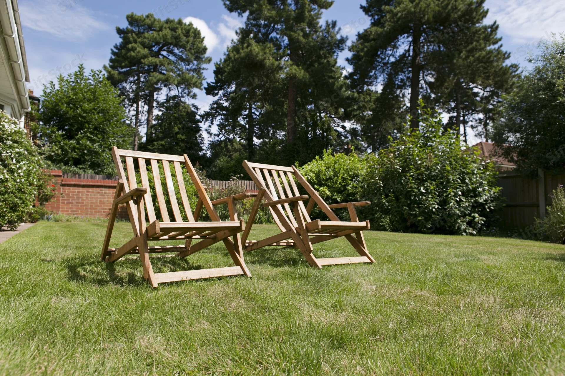 Two wooden deck chairs resting on a neatly trimmed green lawn in a private backyard garden