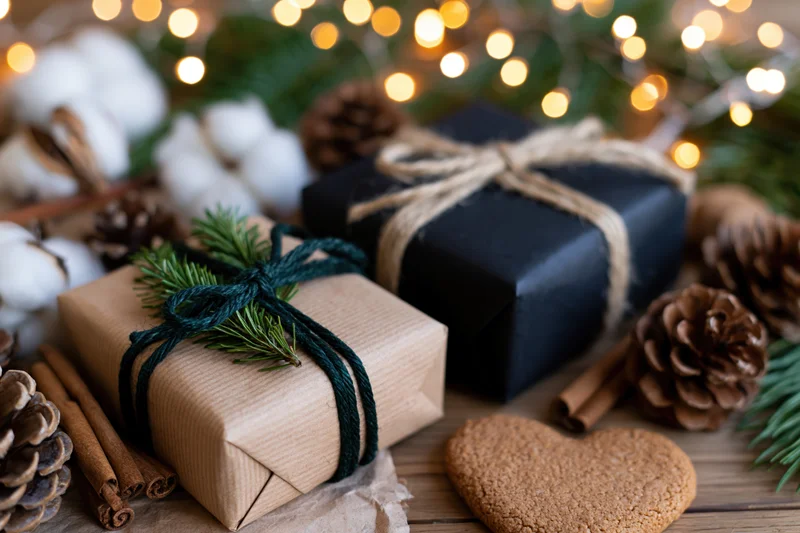 Two wrapped christmas gifts on wooden surface with pinecones and lights