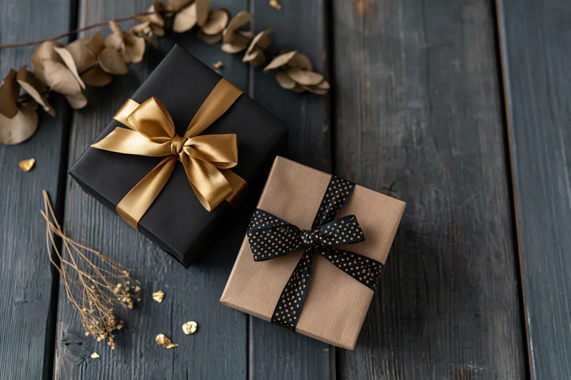 Two wrapped gift boxes with ribbons and dried flowers on dark wooden surface