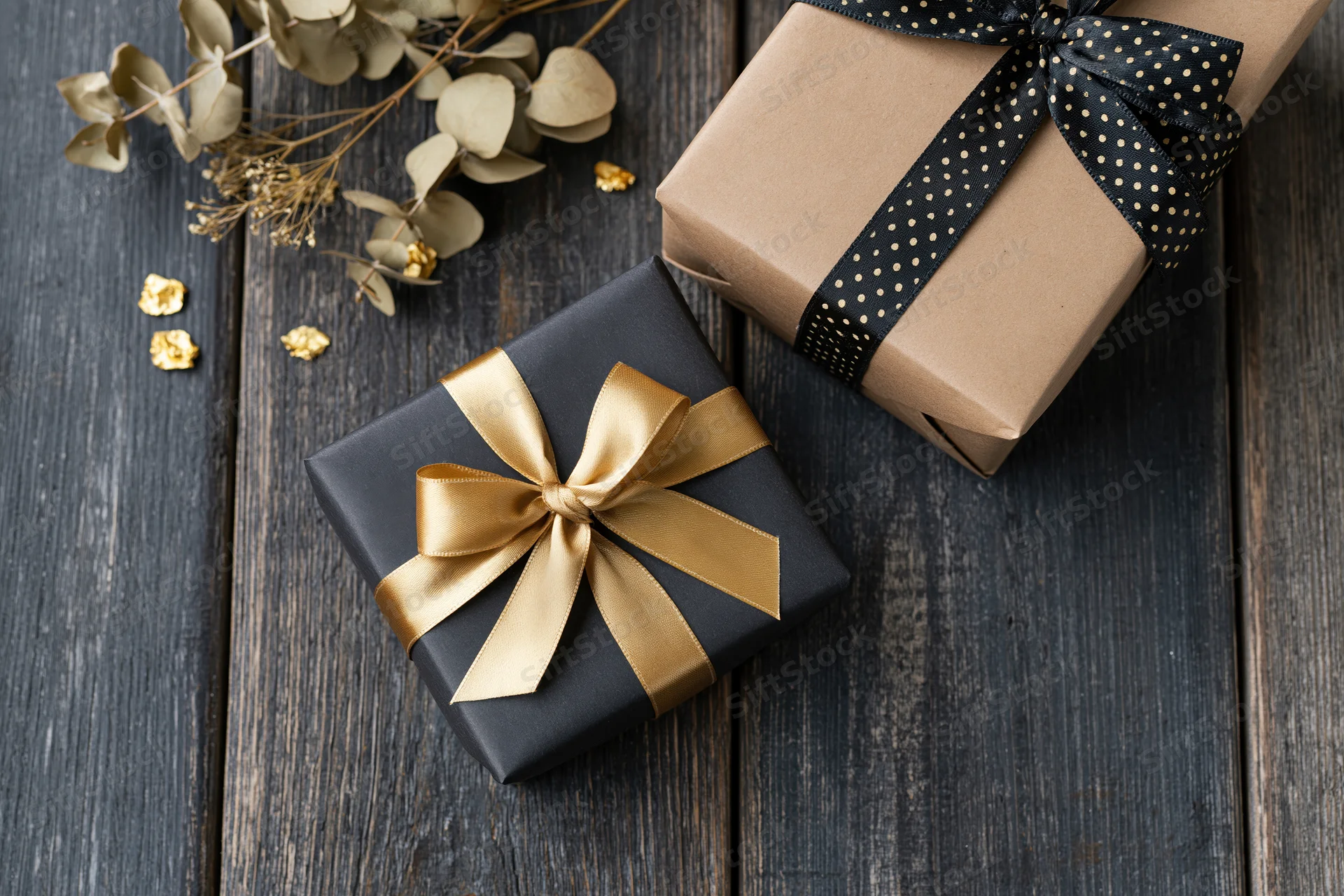 Two wrapped gift boxes with ribbons and dried foliage on dark wooden surface