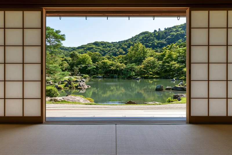 View through open shoji sliding doors onto a tranquil Japanese garden with pond and forested hills