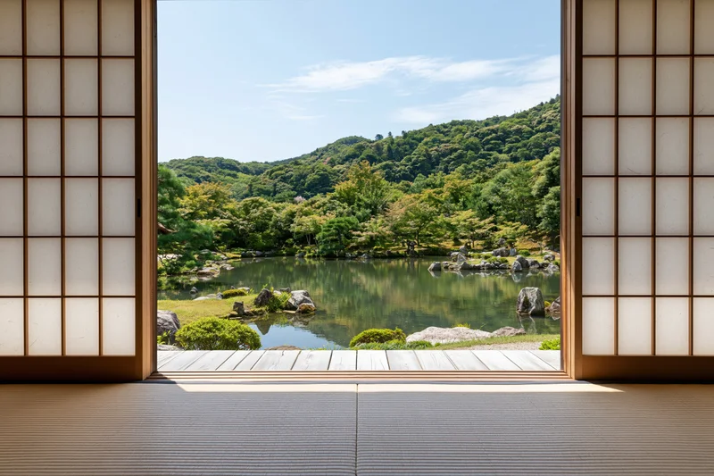 Open shoji doors framing a traditional japanese garden with pond and green hills viewed from tatami floor interior