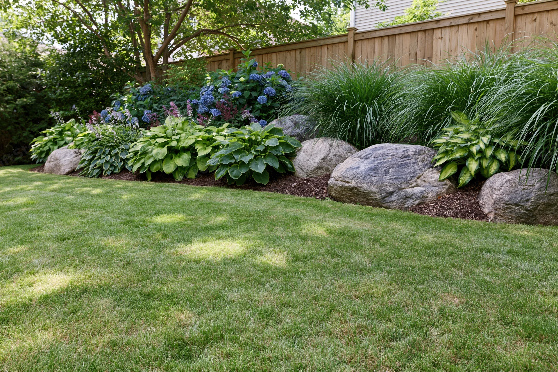 Well-maintained suburban backyard lawn with flower beds and rocks along a wooden fence