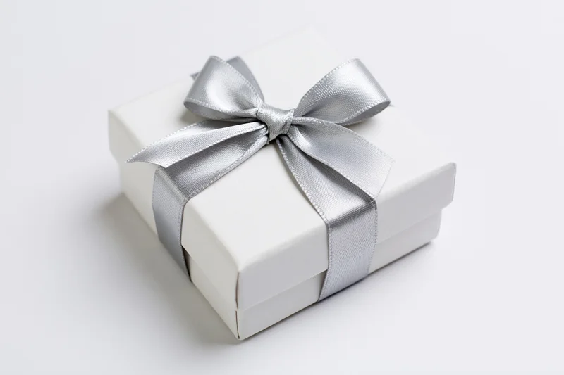 White gift box wrapped with silver satin ribbon on plain white surface