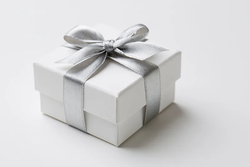 White gift box wrapped with silver satin ribbon on plain white surface