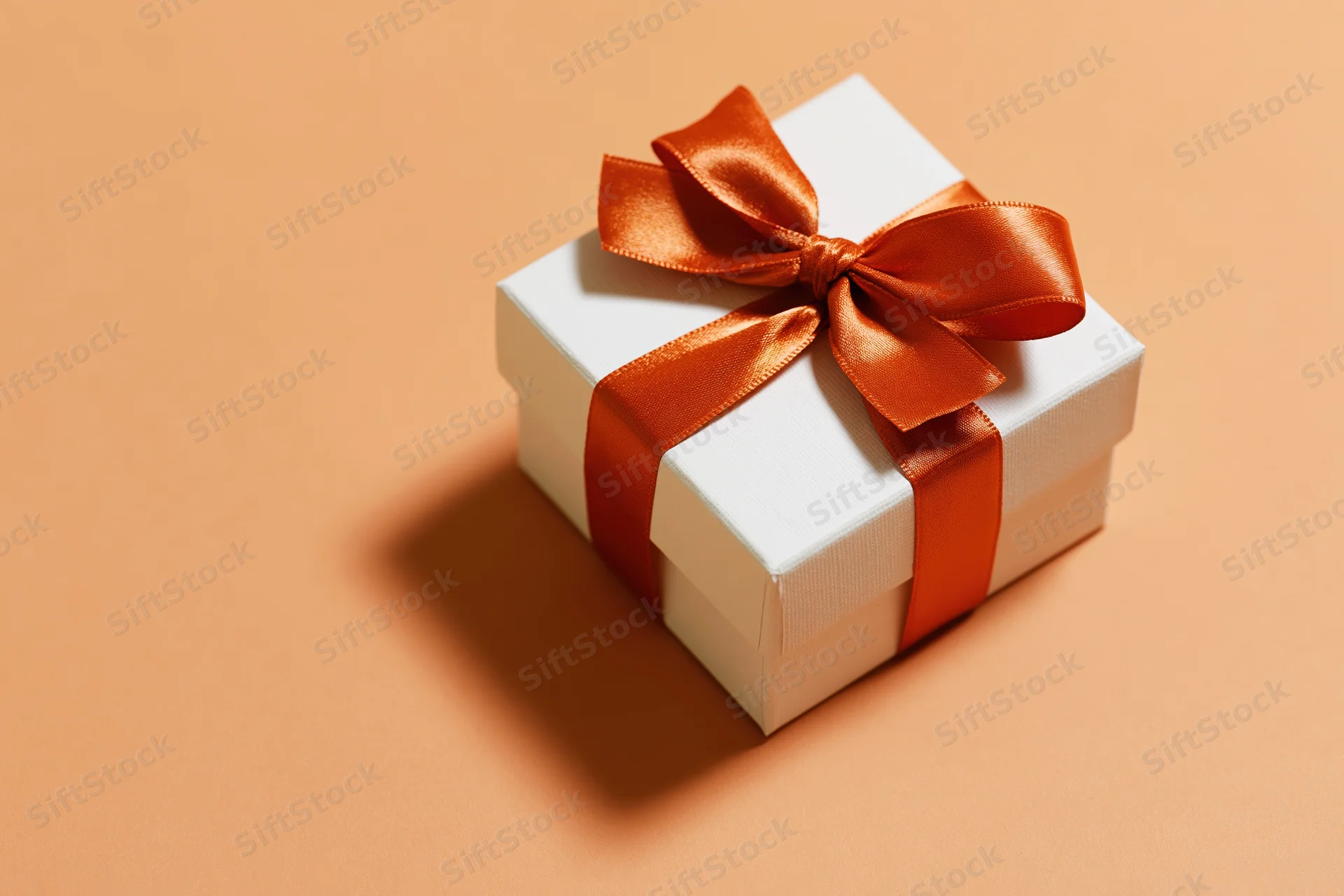 White gift box tied with a glossy burnt-orange satin ribbon on a beige surface