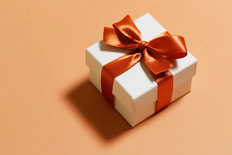 White gift box tied with a glossy burnt-orange satin ribbon on a beige surface