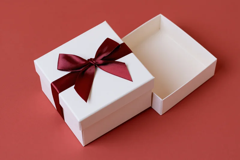 White gift box with red satin ribbon bow open on red surface