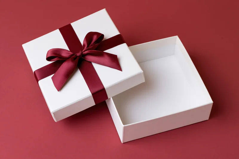 Open white gift box with red satin ribbon bow on red surface