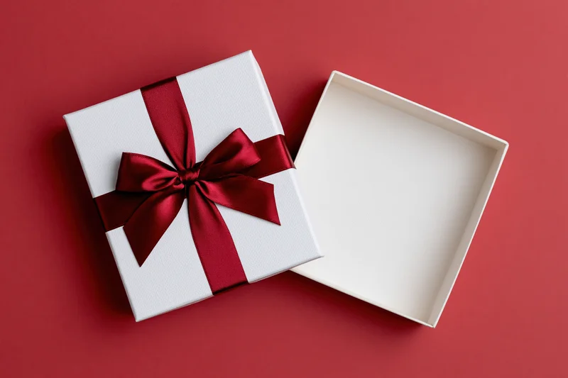 White gift box with red satin ribbon bow open on red surface