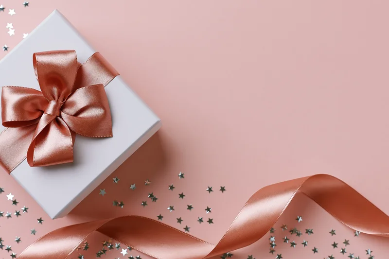 White gift box with rose gold satin bow and scattered stars on pink surface