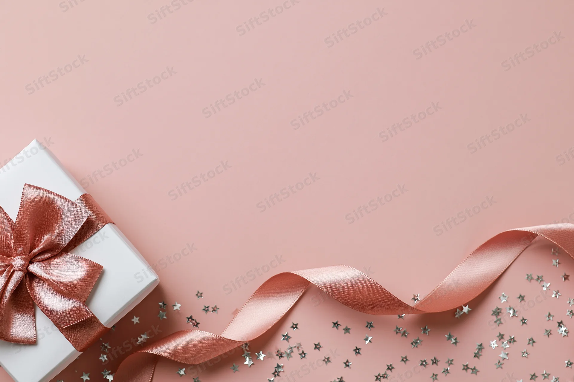 White gift box with rose-gold satin bow and scattered silver stars on pink background