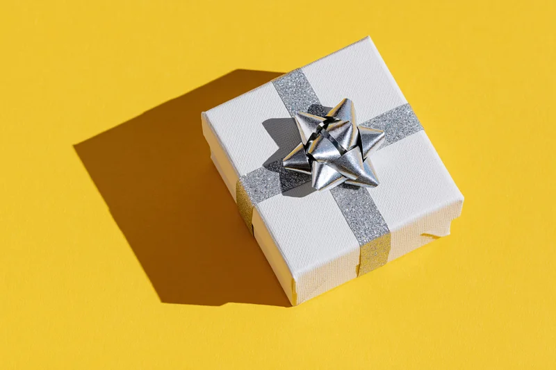 White gift box with silver glitter ribbon and star bow on yellow background