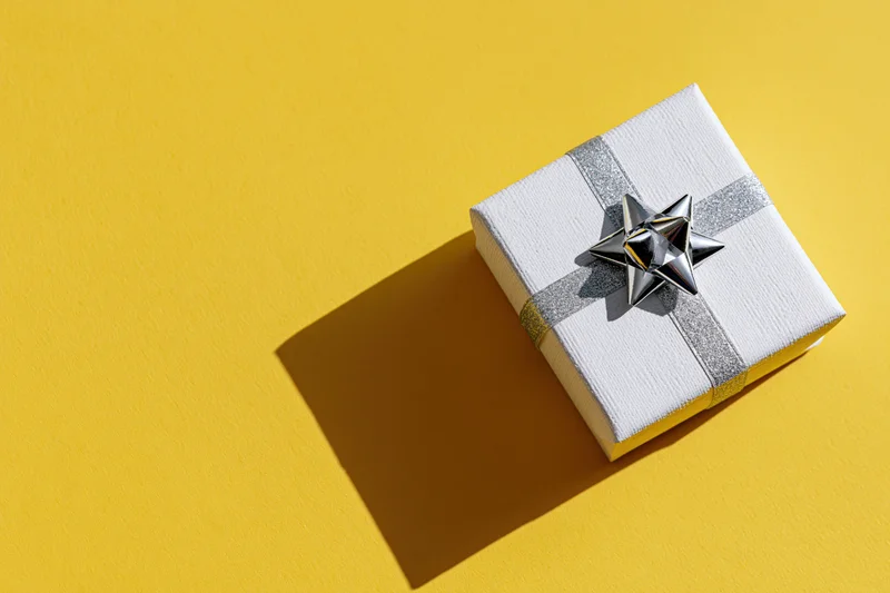 White textured gift box with silver glitter ribbon and star on yellow surface