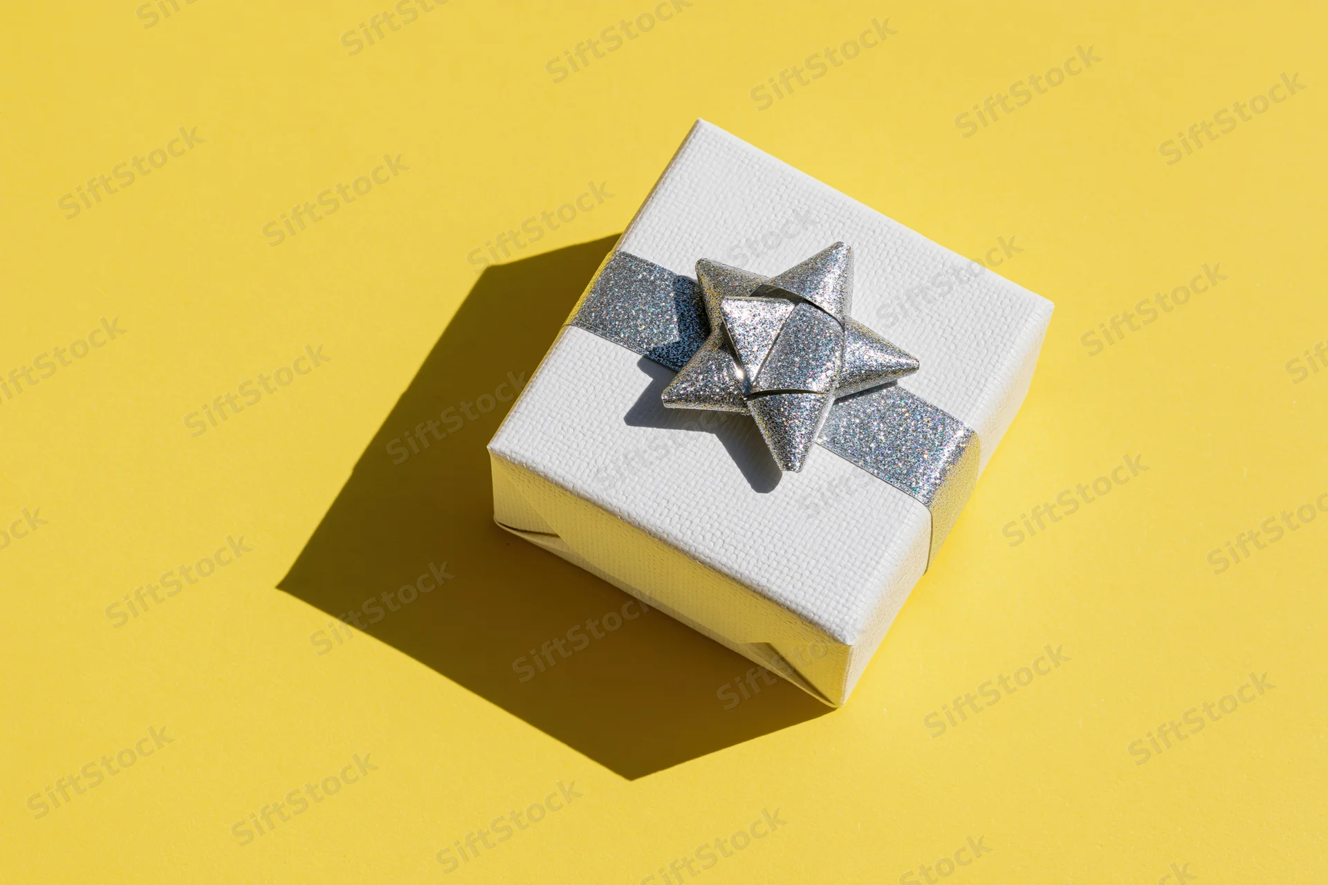 White textured gift box with silver glitter ribbon and star on yellow background