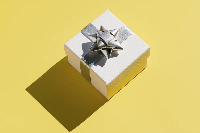 White textured gift box with silver glitter ribbon and star on yellow background