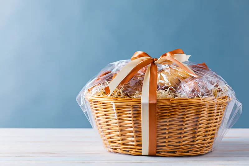 Wicker gift basket wrapped in cellophane with ribbon on a white table against blue background