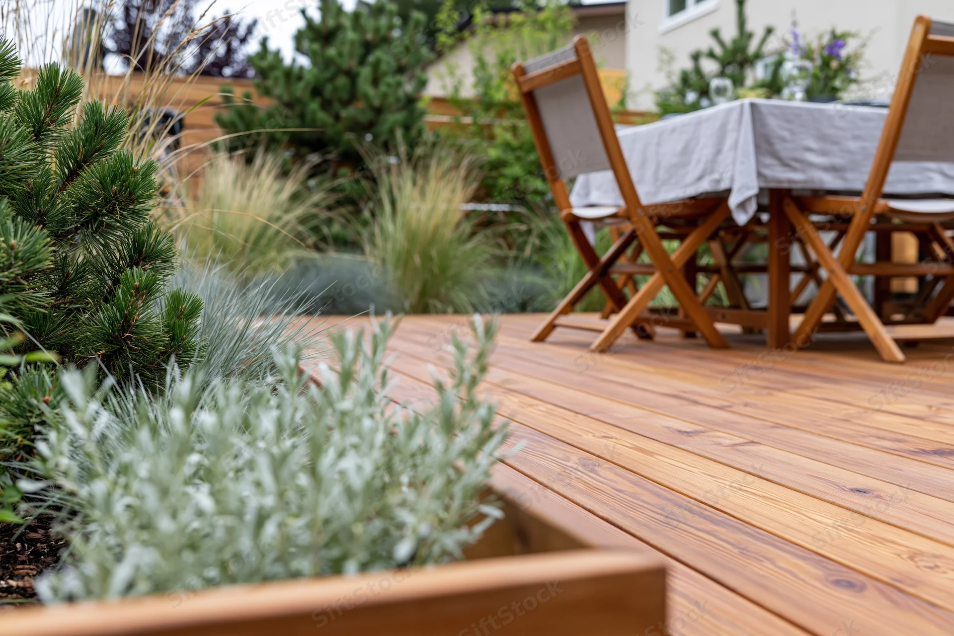 Wooden deck patio with folding chairs around a linen-draped table surrounded by garden plants