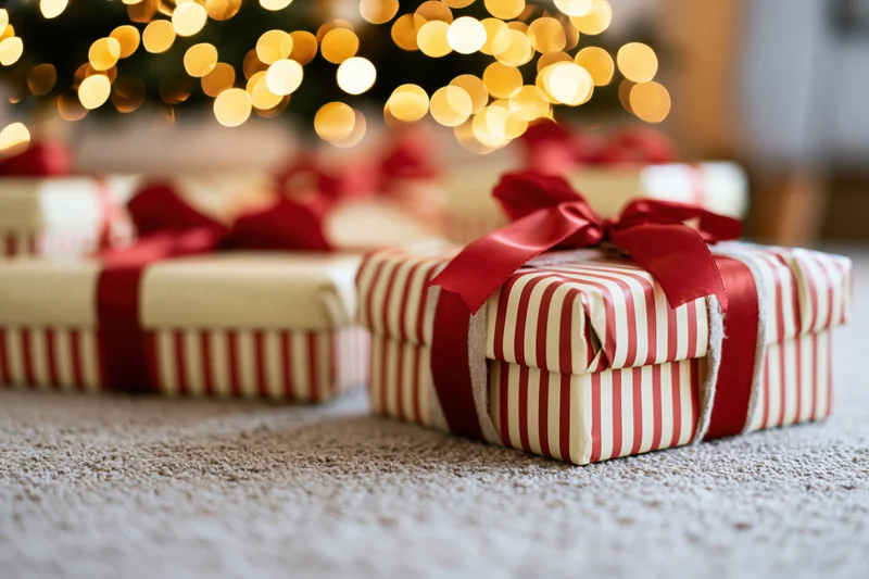 Wrapped gift boxes with red ribbon bows on carpet under christmas tree lights