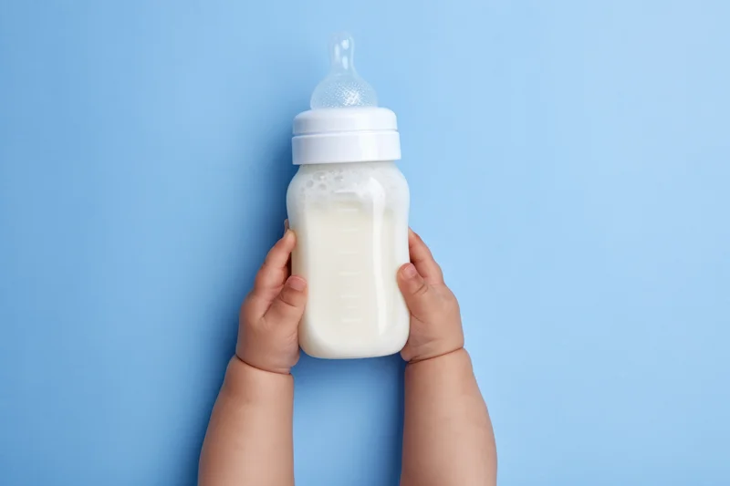 Baby hands holding a milk-filled bottle with measurement marks against a blue background
