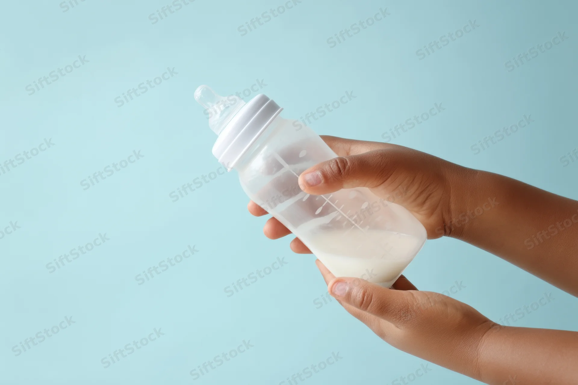 Hands holding a baby bottle with milk and measurement marks against a light blue background