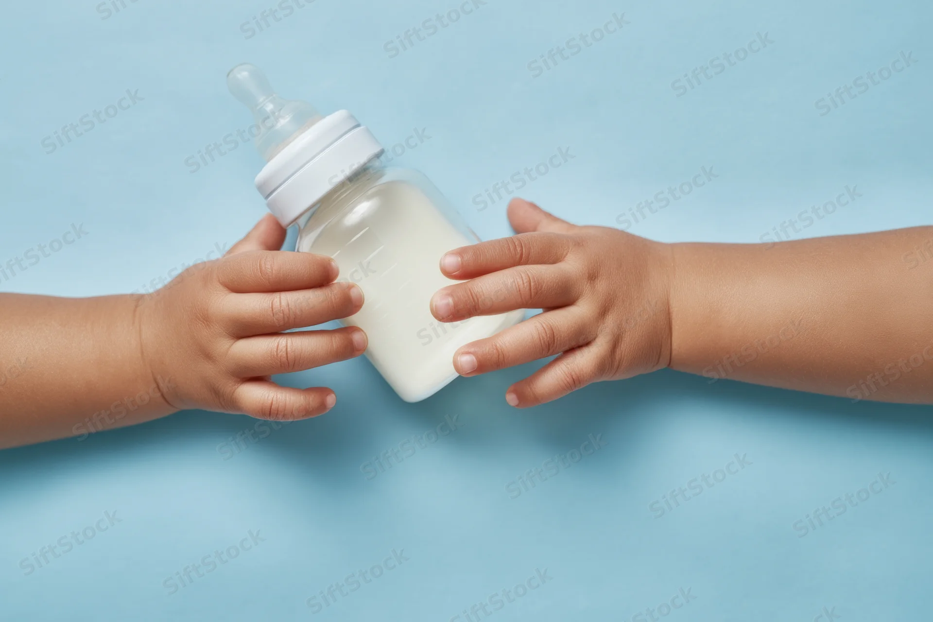 Baby bottle with milk held by infant hands against blue background
