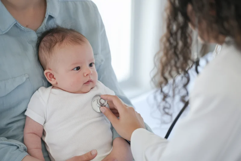 Baby being examined with stethoscope by doctor while held by parent in clinic