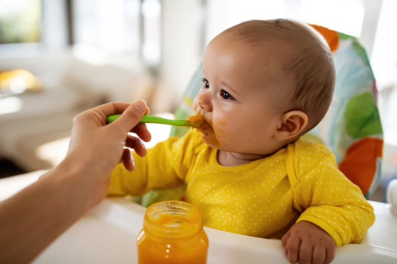 Baby in yellow polka-dot onesie being fed with spoon in high chair