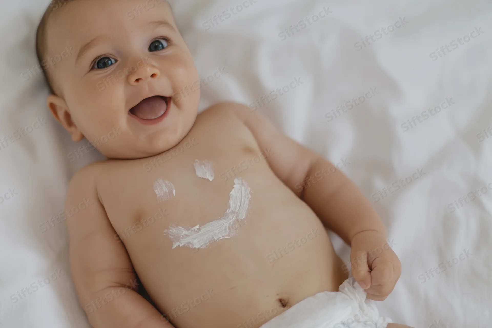 Baby lying on white sheet with smiley face painted on chest, smiling widely
