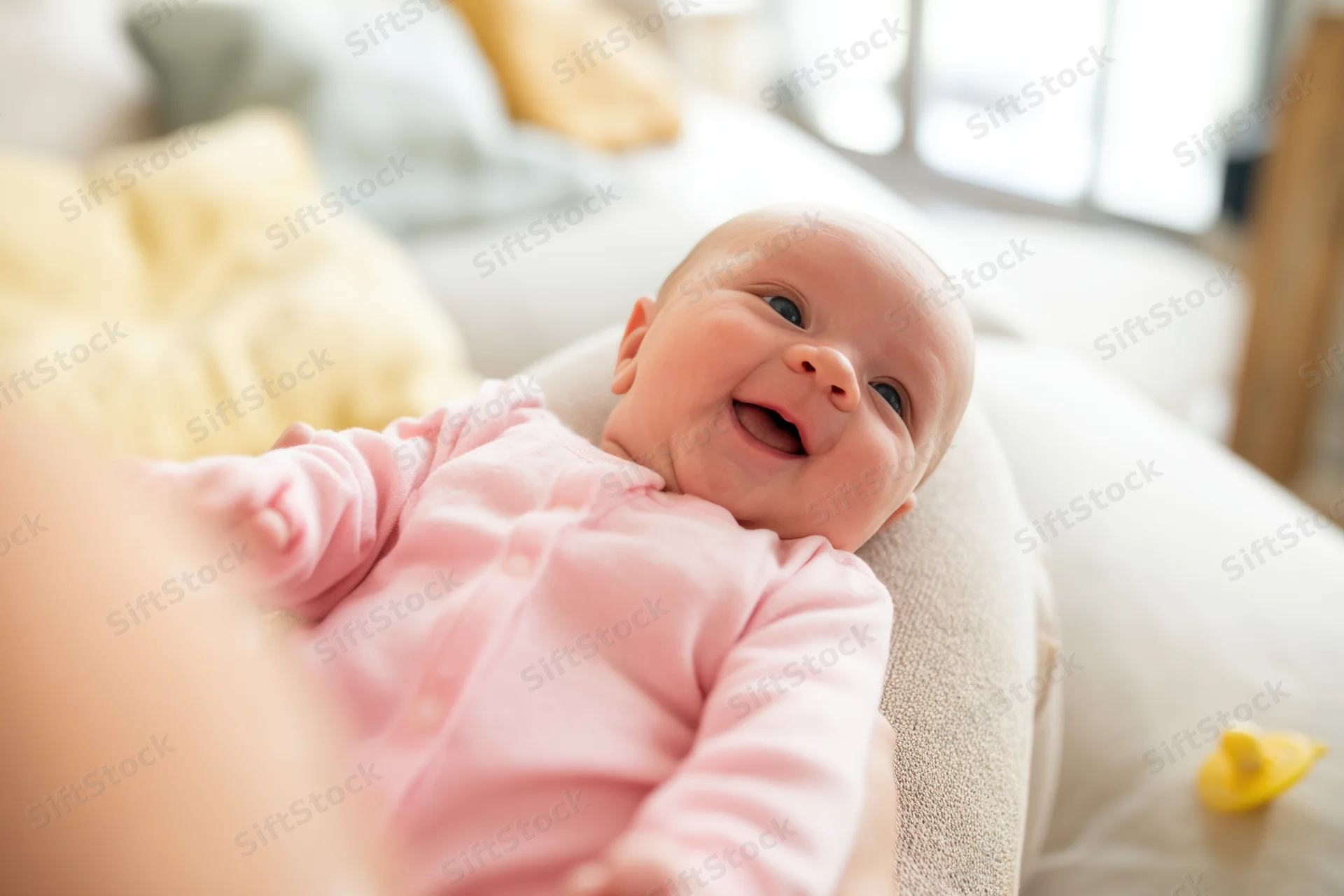 Baby lying on adult's lap on couch smiling in living room