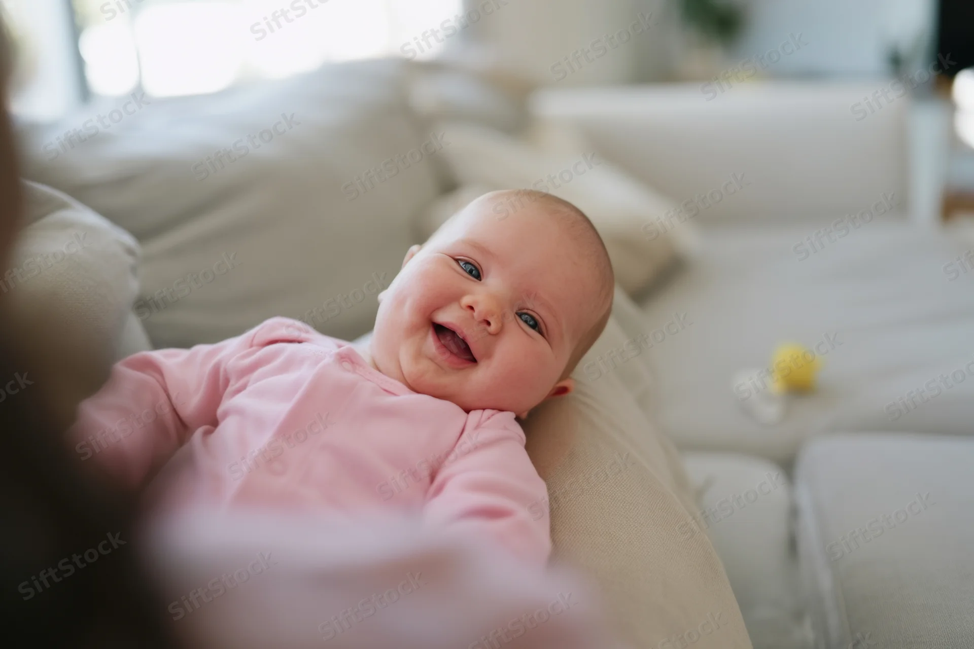 Baby lying on adult's lap on a couch in a cozy living room smiling widely