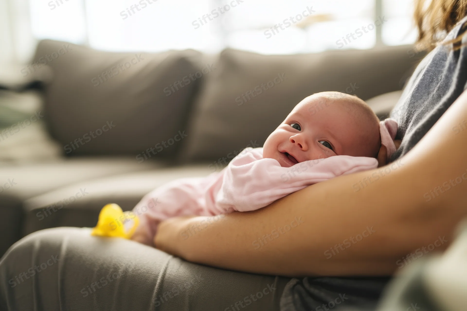 Baby smiling while lying on mother's lap on a couch in a living room