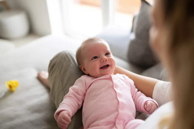 Smiling baby lying on mother's lap on a cozy living room couch