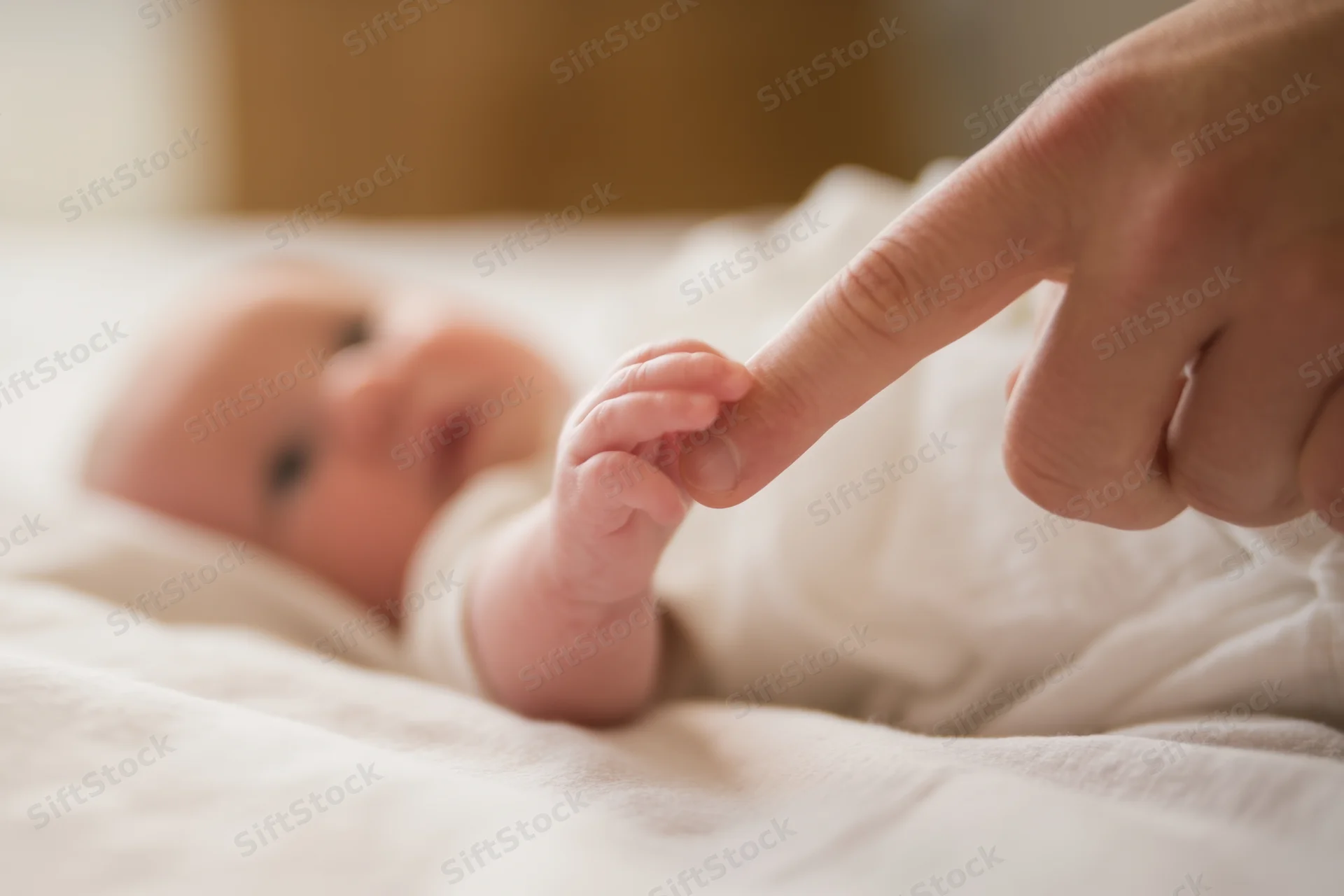 Newborn baby lying on soft blanket reaches to grasp adult finger