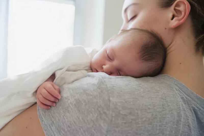 Sleeping baby nestled on mother's shoulder indoors