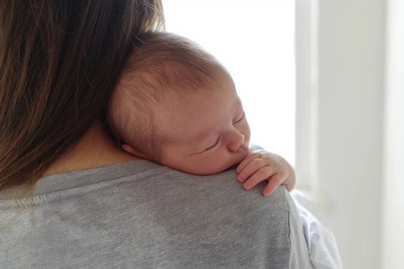 Newborn baby sleeping on caregiver's shoulder indoors