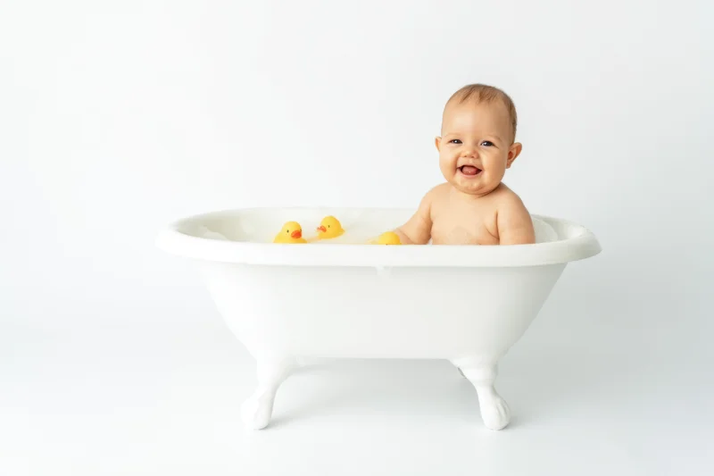 Baby laughing in a white clawfoot bathtub with rubber ducks