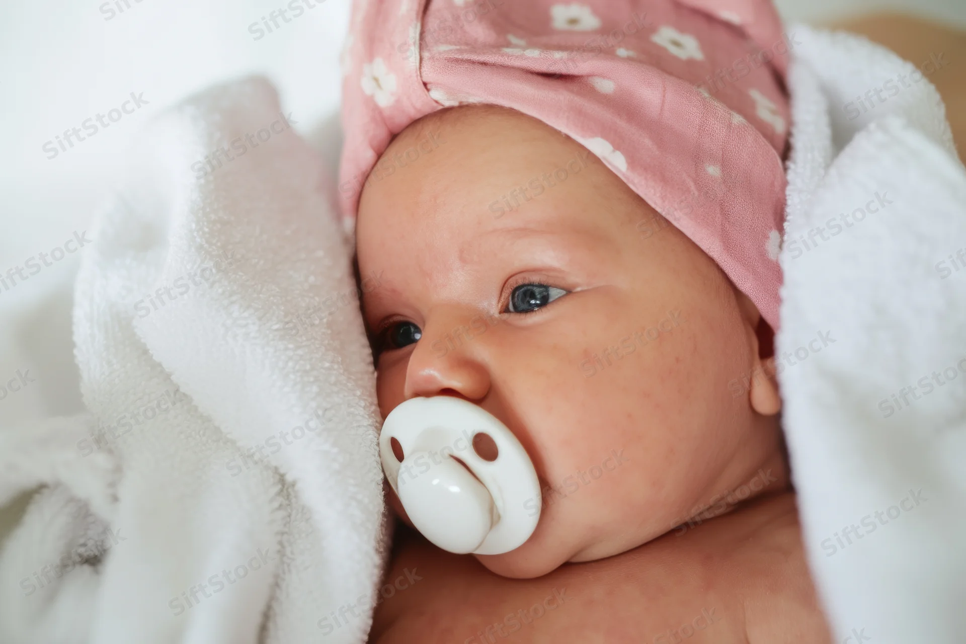 Newborn baby with pink floral towel headwrap and pacifier wrapped in white blanket