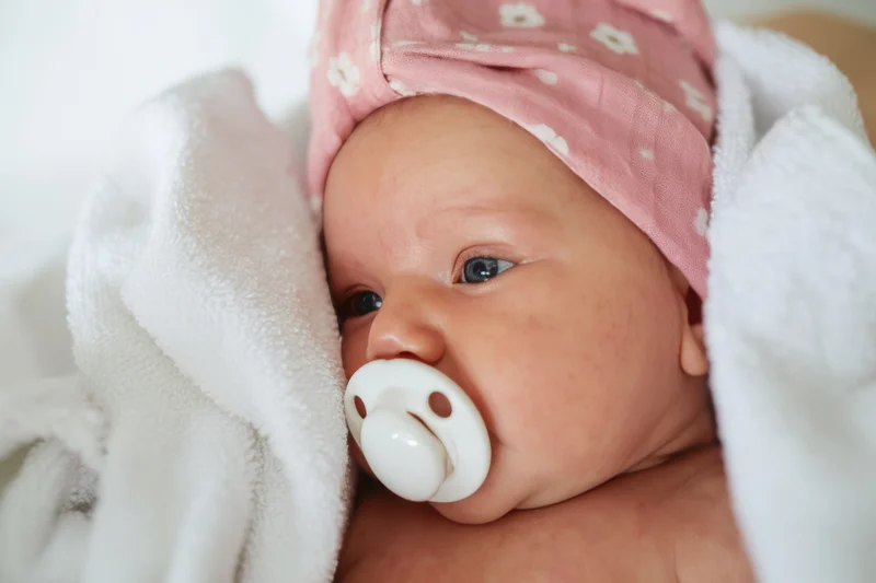 Newborn baby with pink floral towel headwrap and pacifier wrapped in white blanket