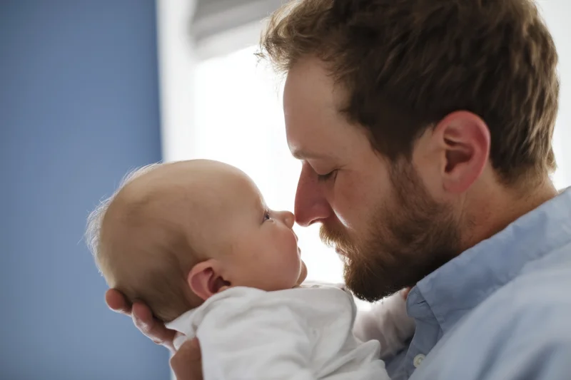 Father cradling newborn baby close to his face indoors