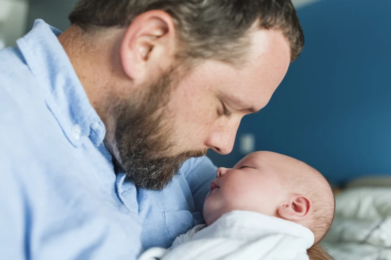 Father cradling newborn baby close to his chest in a quiet indoor setting